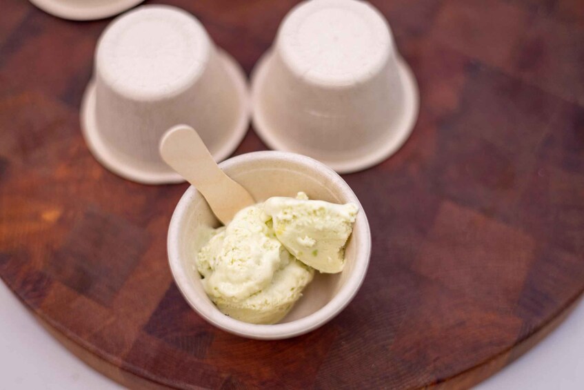 A bowl of ice cream with a spoon, placed on a wooden tray with two cups in the background. 5