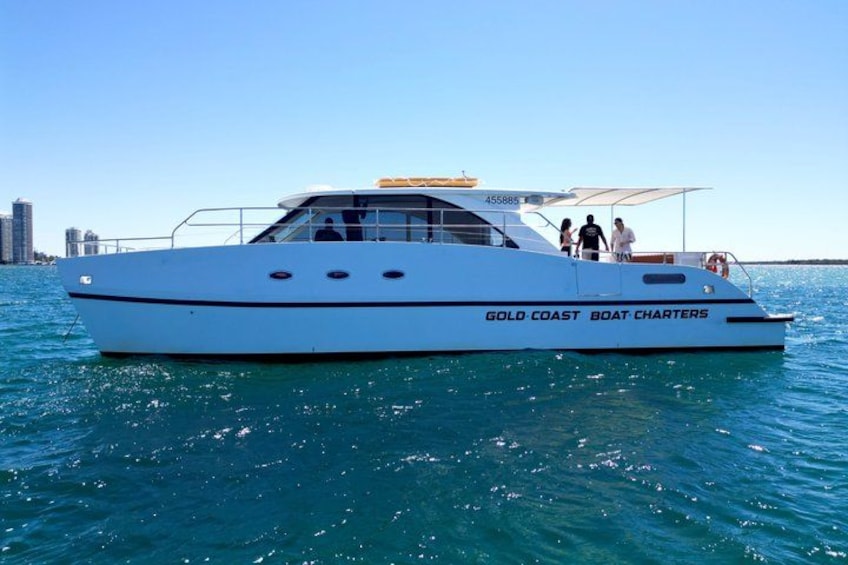A white yacht named 'GOLD COAST BOAT CHARTERS' with a city skyline in the background. 1
