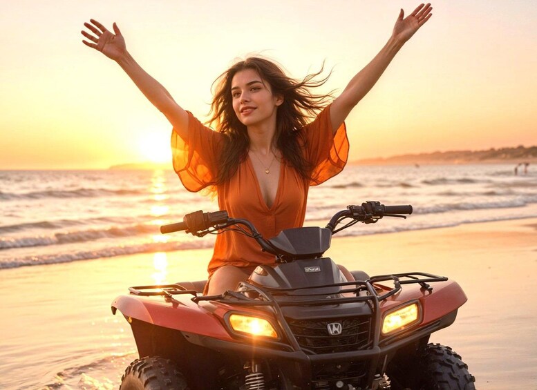 A person on a red ATV with arms raised, on a beach at sunset. 1
