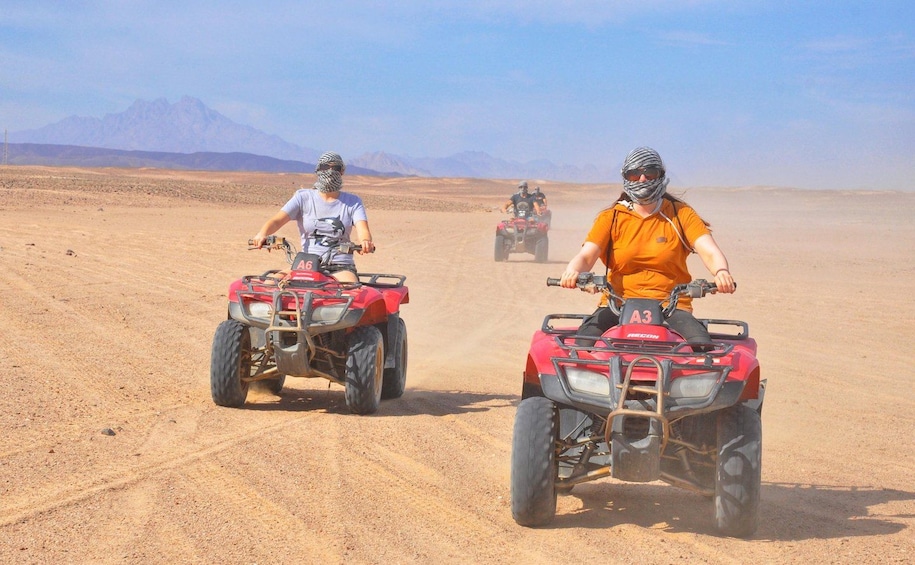 Two people riding ATVs on a desert road with mountains in the background. 4