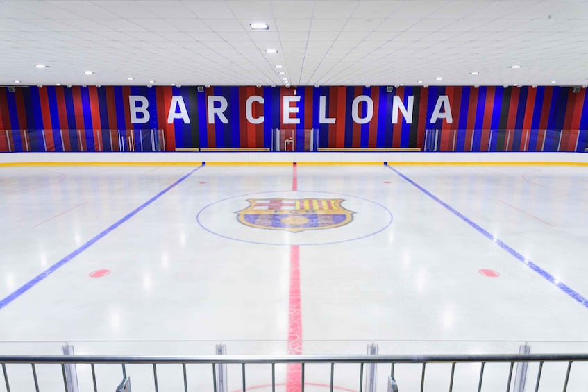 An indoor ice hockey rink with the word 'BARCELONA' on the wall and the team's logo on the ice. 3