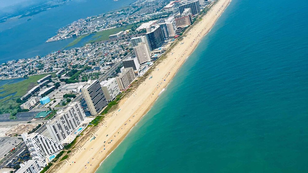 An aerial view of a coastal city with a long sandy beach, high-rise buildings, and a clear blue ocean. 1