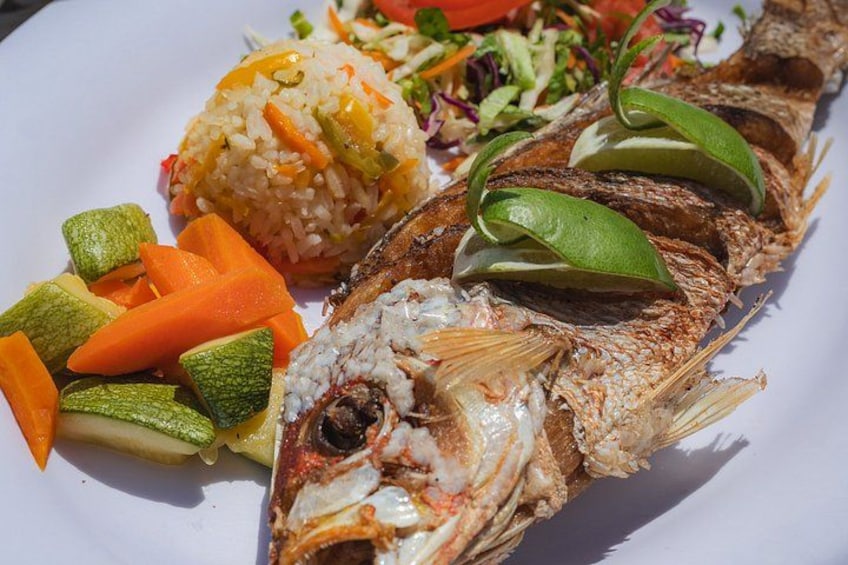 A whole grilled fish with rice and vegetables on a plate. 3