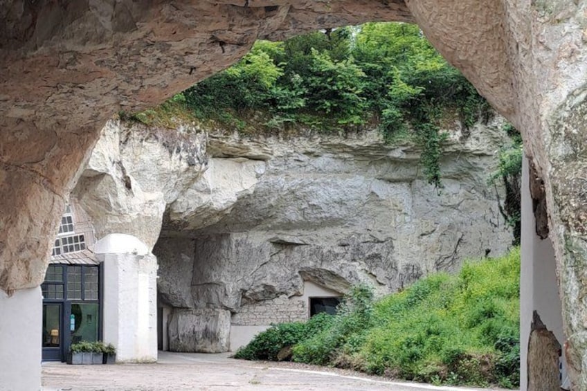 A rock archway with greenery growing on top, a building entrance, and a pathway. 1
