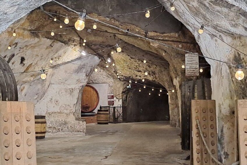 An underground wine cellar with wooden barrels, stone walls, and string lights. 3