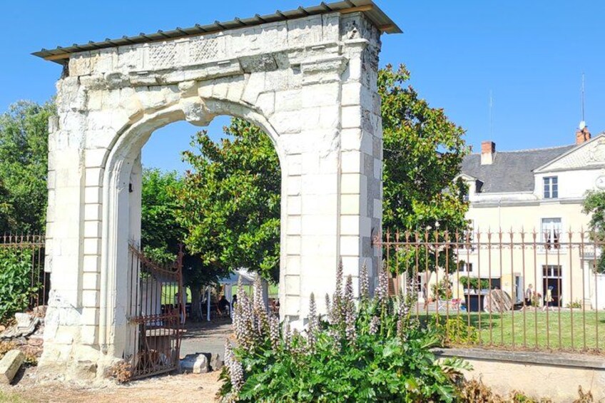 A stone archway with a metal gate, surrounded by greenery and a white building in the background. 5