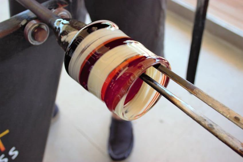 A glass blowing process with a red and white object being shaped by metal rods. 2