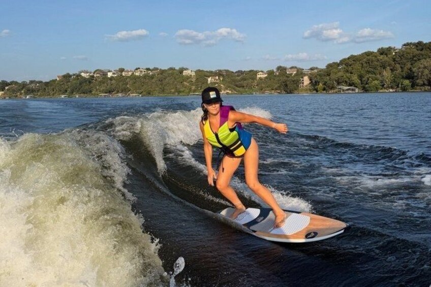 A person wakeboarding on a body of water with waves, surrounded by a hilly landscape with houses. 1