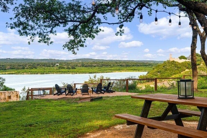 A lakeside picnic area with chairs and a table, surrounded by greenery and a view of a lake. 2