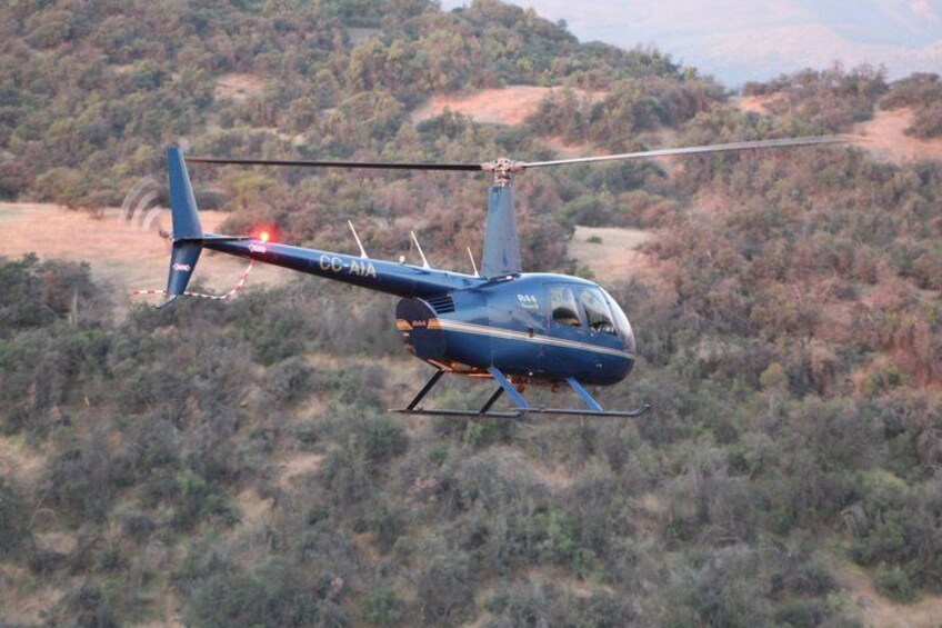 A blue helicopter with the registration number CC-AJA flying over a hilly, forested landscape. 5