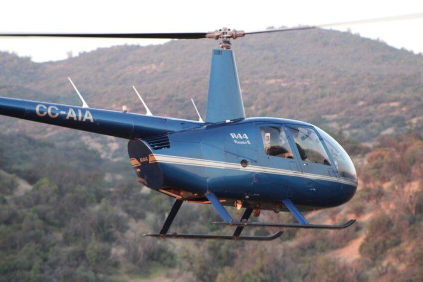 A blue helicopter with the registration number R44 flying over a mountainous landscape. 3