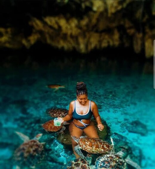 A person in a blue swimsuit sitting on the ocean floor with sea turtles around. 2