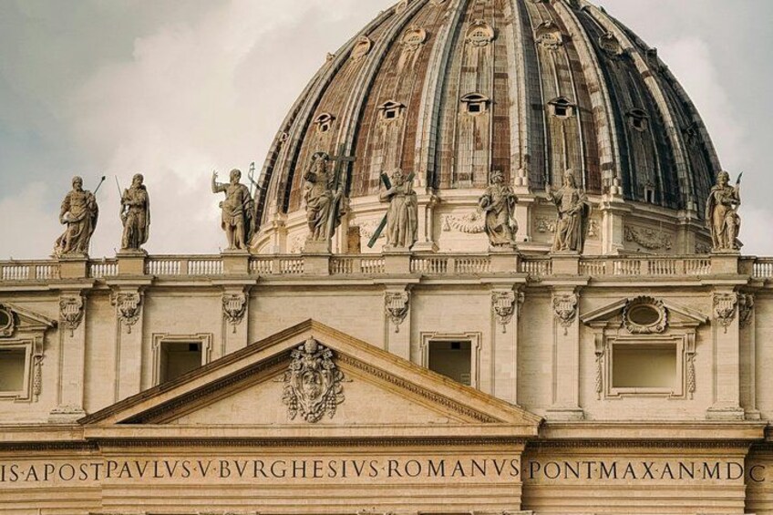 A large dome with statues on top, a prominent crest, and inscriptions on the facade. 3