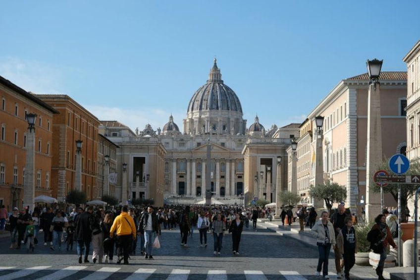 A busy square with a large historical building featuring a dome in the background. 1