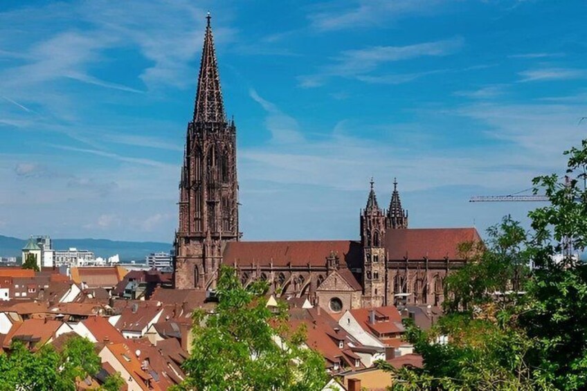 A cathedral with a tall spire and two smaller towers, surrounded by a cityscape with red-roofed buildings. 2