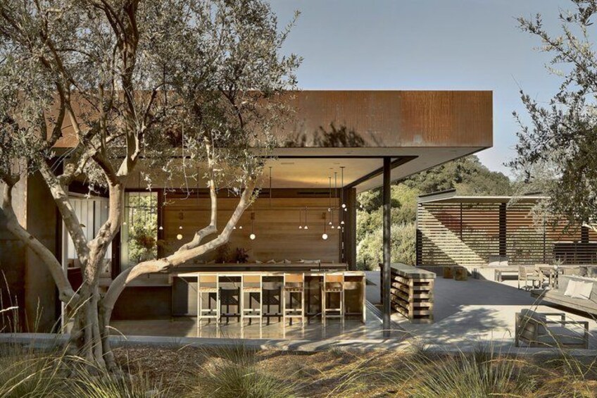 A modern house with a wooden exterior, a covered outdoor seating area, and a staircase leading to a deck. 4