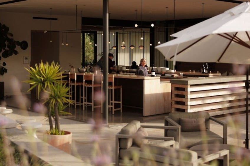 An outdoor seating area with a bar and tables, surrounded by plants and umbrellas. 3