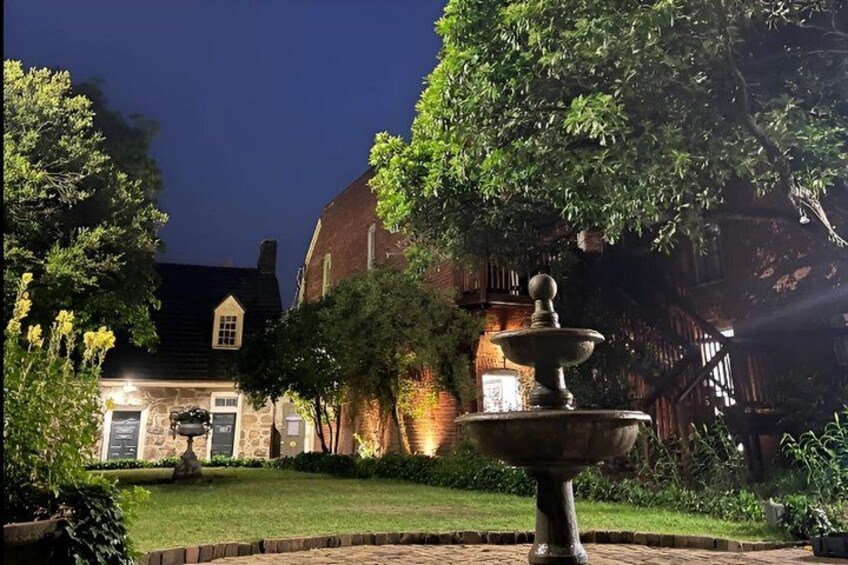 A well-lit fountain in a garden with a brick building in the background. 3