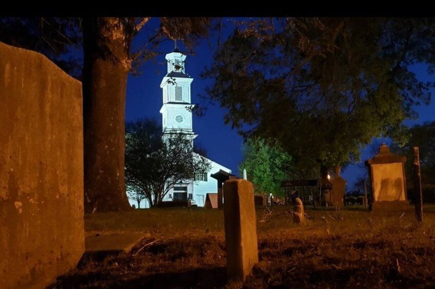 A church with a bell tower, surrounded by gravestones and trees. 4