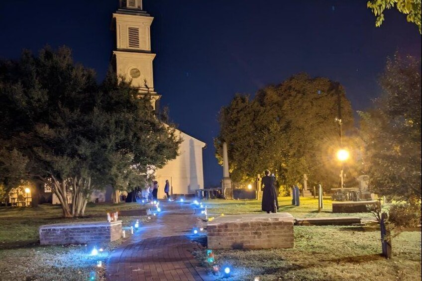 A nighttime scene with a church, a pathway lit by blue lights, and trees. 2