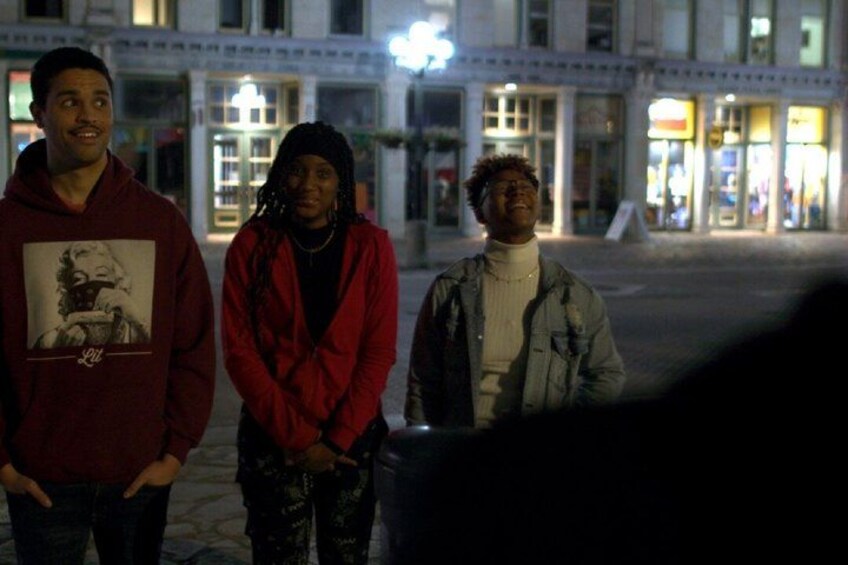 Three people standing on a city street at night. 1