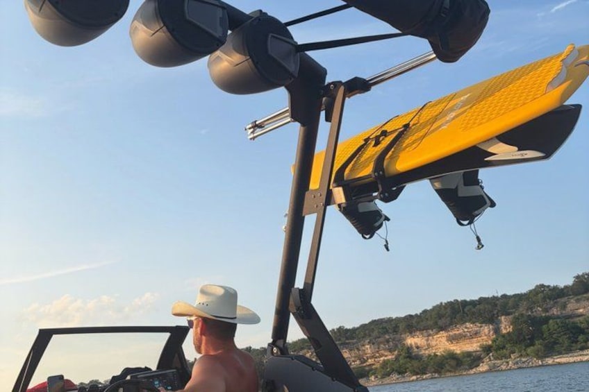 A person in a white hat steering a boat with a yellow surfboard attached to the side. 5