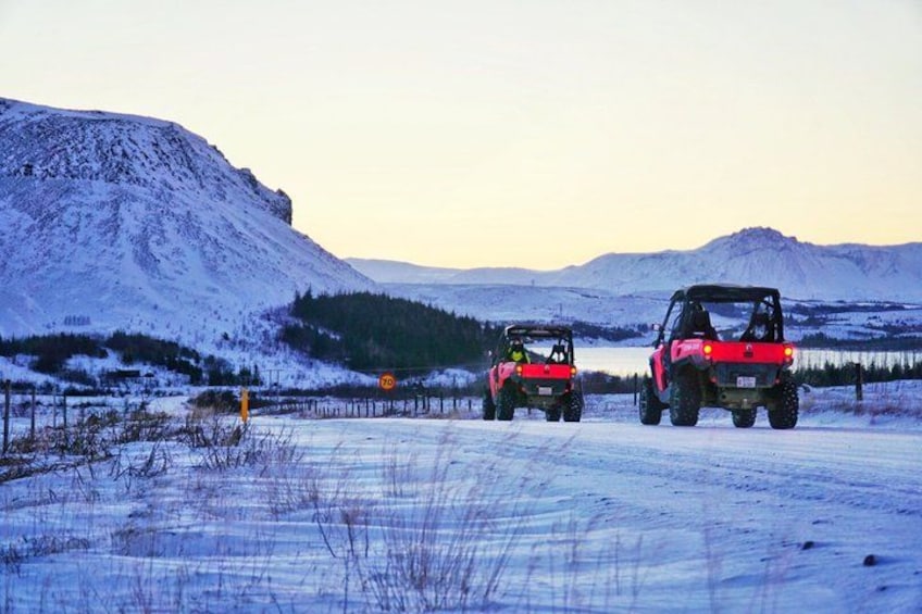 Two off-road vehicles on a snow-covered road with mountains in the background. 2