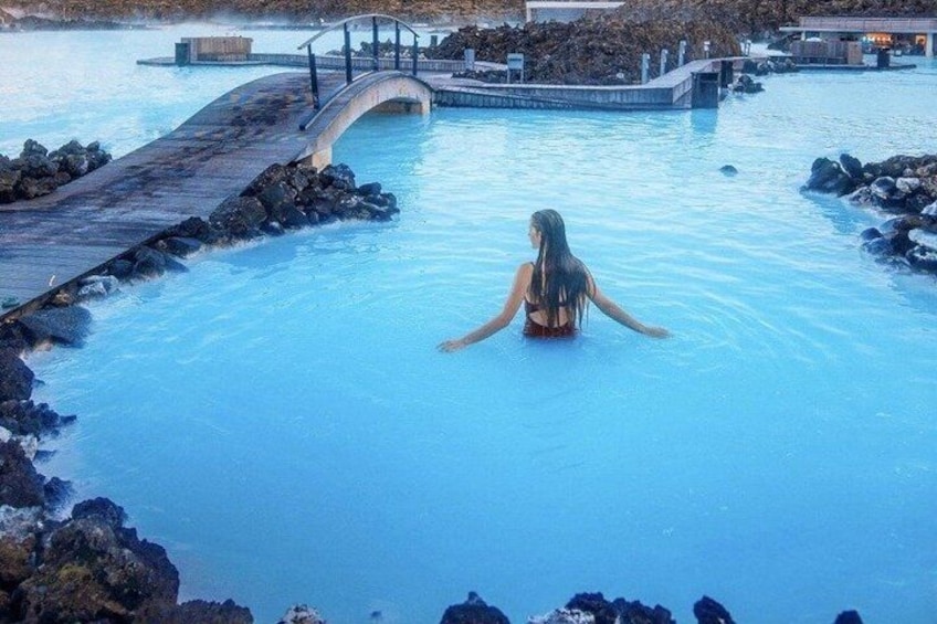 A person in a geothermal pool surrounded by rocks and a bridge. 1