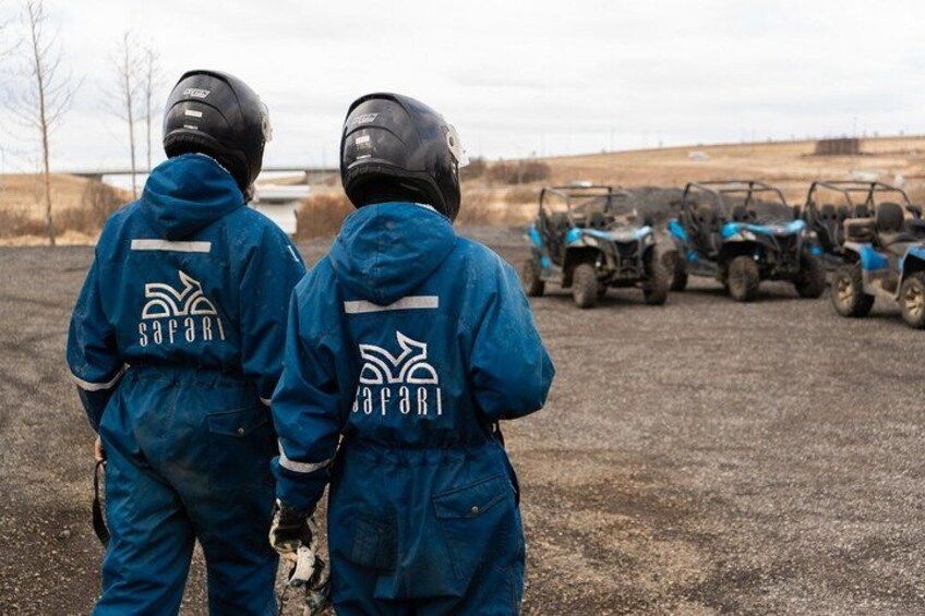 Two people in safari gear standing in a field with ATVs in the background. 5