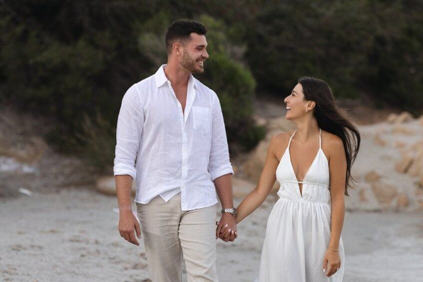A couple holding hands on a sandy beach with greenery in the background. 4