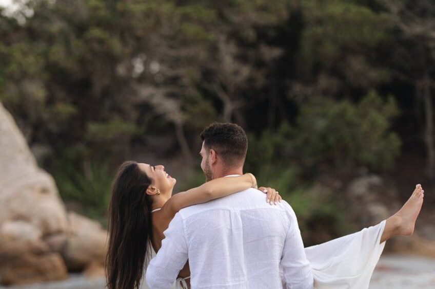 A couple embracing by a rocky shoreline with trees in the background. 5