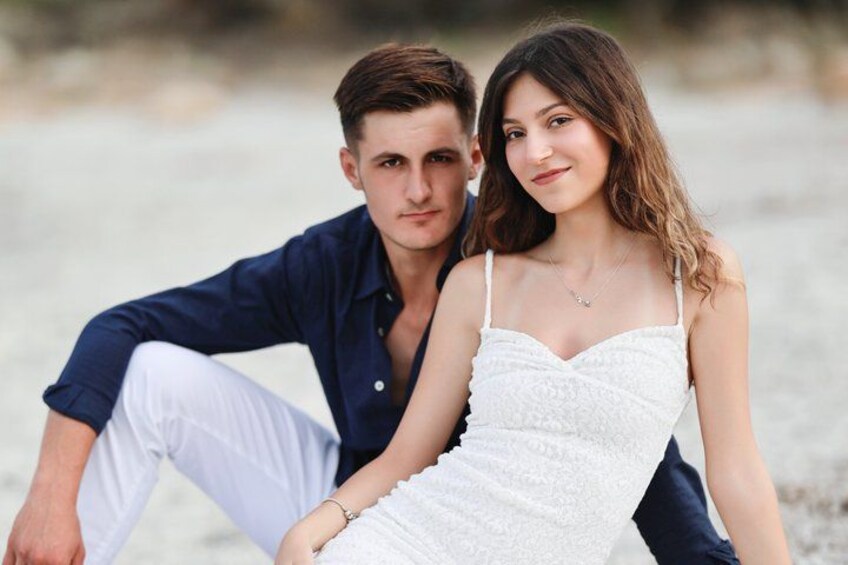 A couple sitting on a beach with sand and water in the background. 3