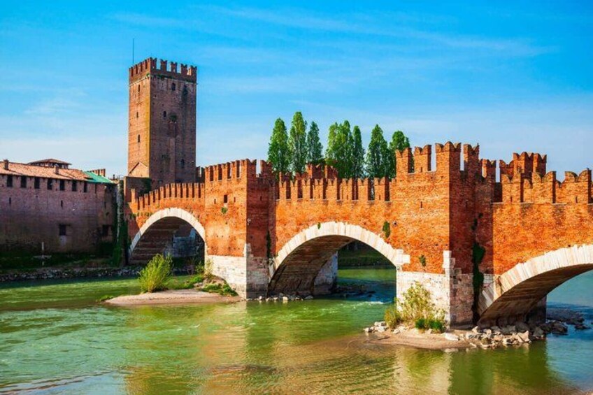 A medieval stone bridge with arches over a river, a tall tower, and a brick wall. 4