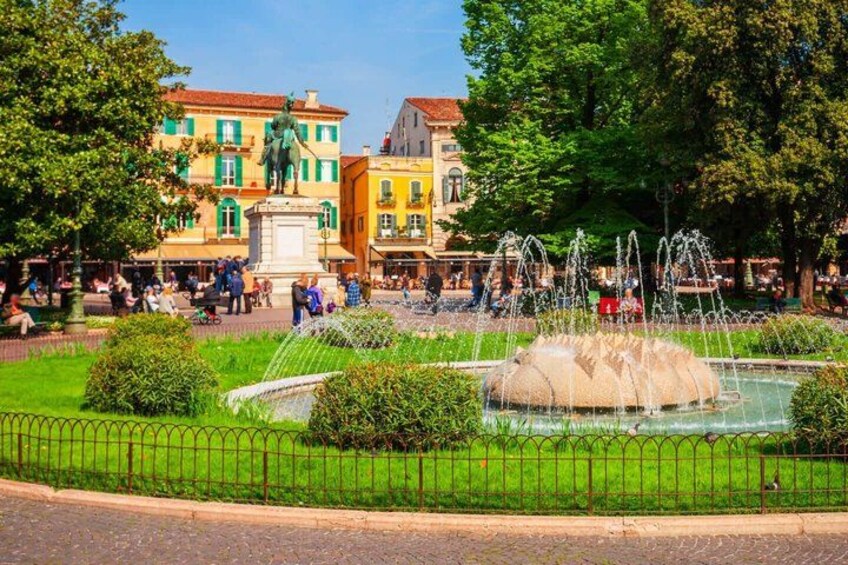 A public square with a fountain, a statue, and colorful buildings in the background. 5