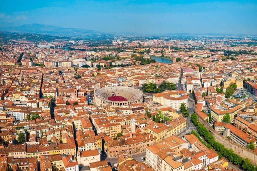 An aerial view of a city with a prominent circular building, likely a historical site, surrounded by densely packed buildings with red-tiled roofs. 1