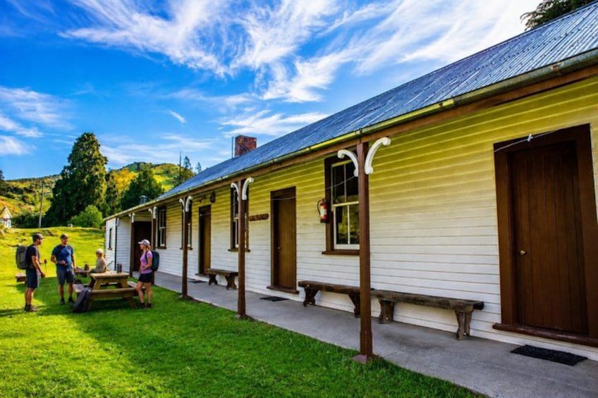 A yellow building with a wooden porch, surrounded by green grass and trees. 3