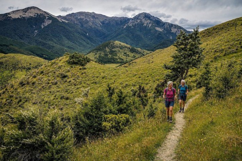 A hiking trail with two hikers, surrounded by green hills and mountains. 5