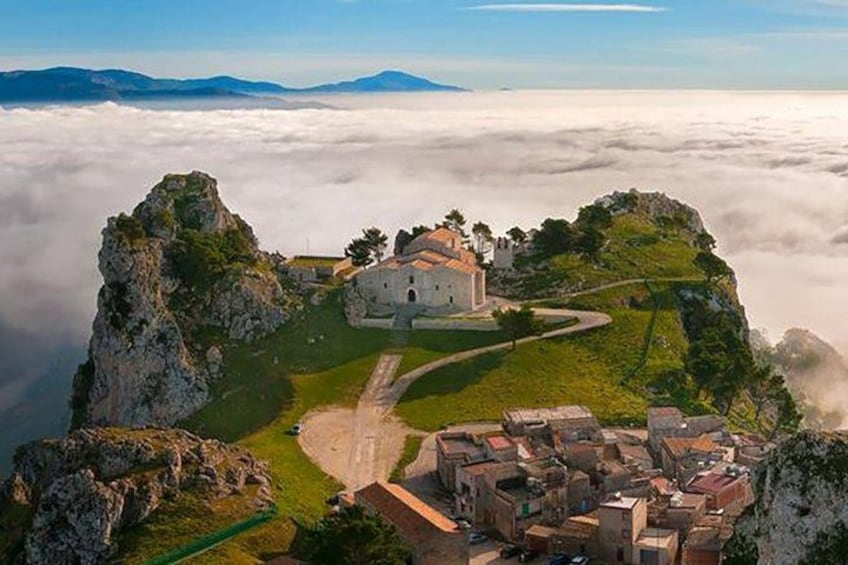 A village perched on a cliff above a sea of clouds, with a prominent church and winding paths. 1