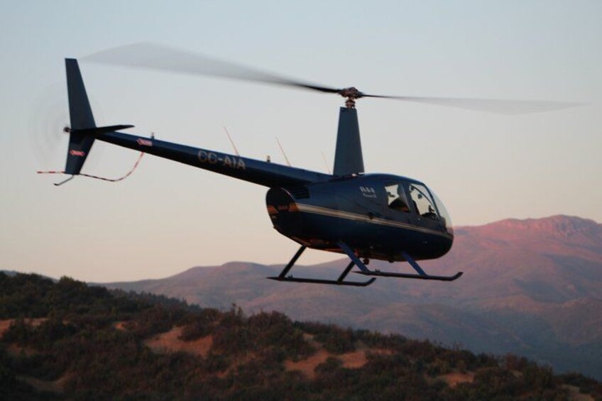 A helicopter with registration number CC-AIA flying over a mountainous landscape. 3