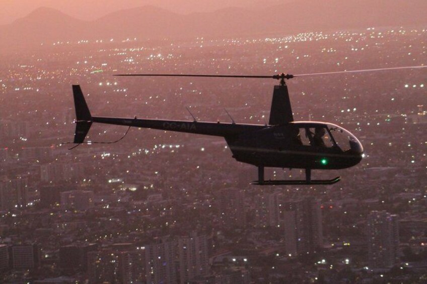 A helicopter flying over a city at dusk with lights visible below. 1
