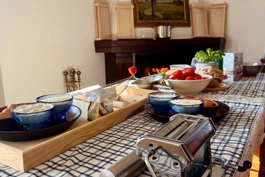 A kitchen with a checkered tablecloth, blue bowls, a grater, and a fire in the background. 1