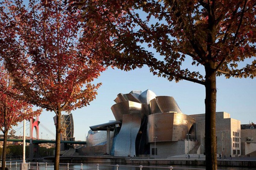 A modern architectural building with a unique, reflective surface, surrounded by trees with autumn leaves. 4