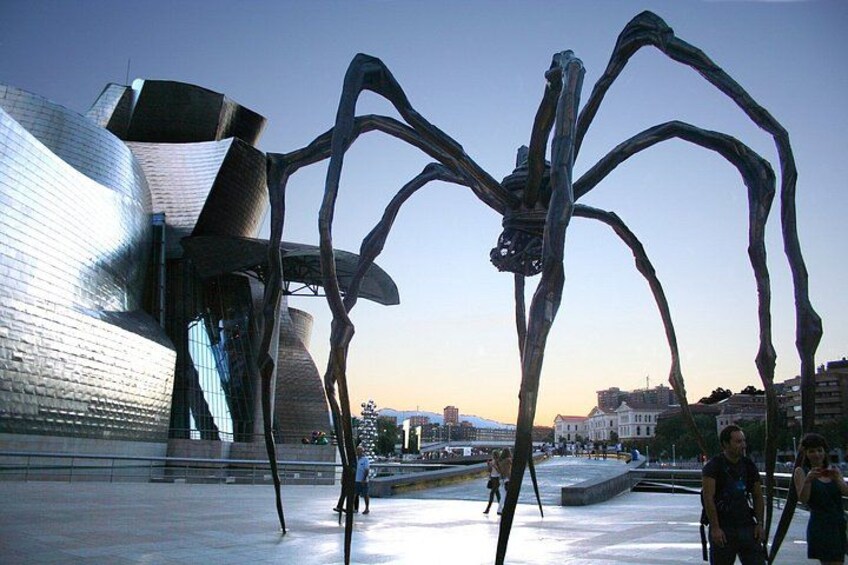 A modern sculpture of a spider in an urban setting with a reflective building in the background. 2