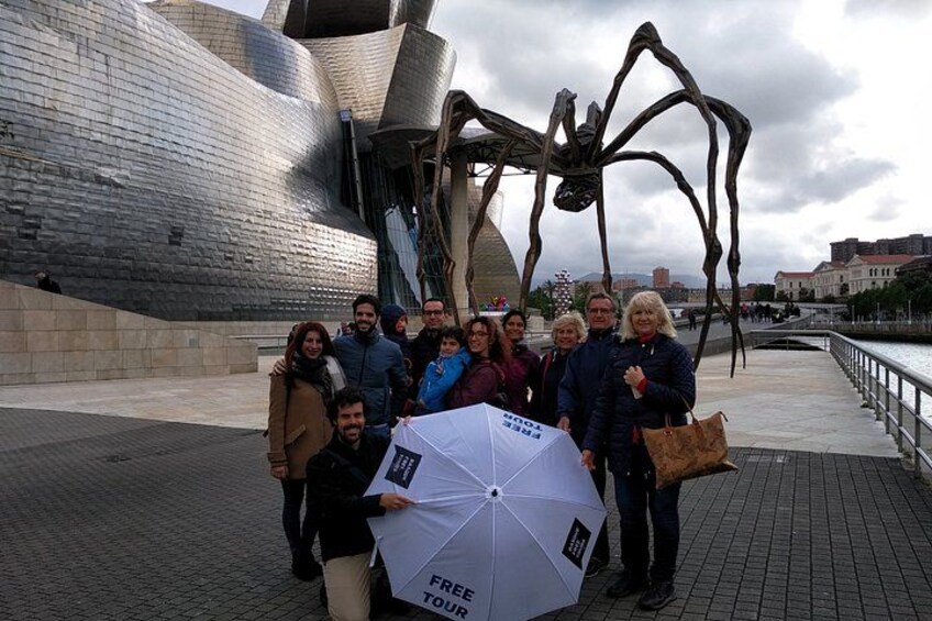 A group of people posing in front of a large metallic sculpture and a modern building. 1