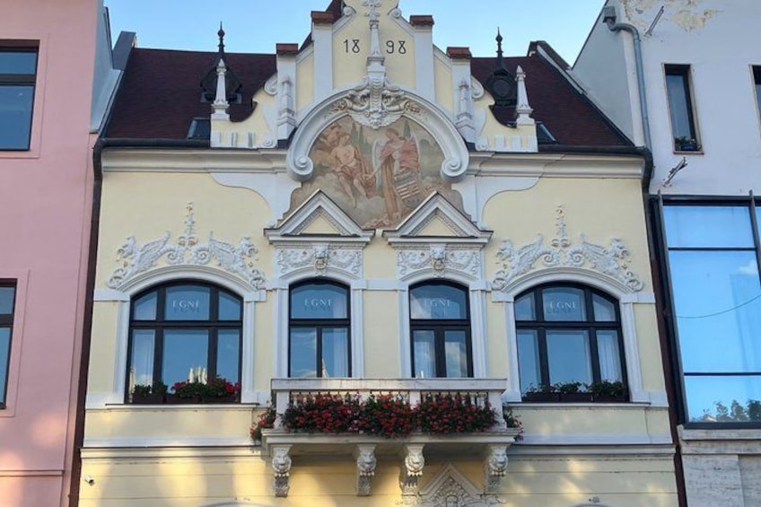 A building with ornate architectural details, including a balcony with flowers and a mural above the windows. 5