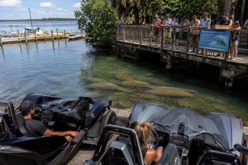 A water tour with people in speedboats, a dock, and a bridge with people watching. 1