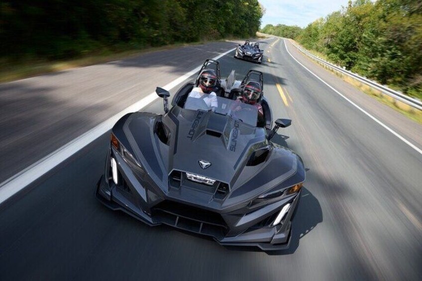 A dark-colored sports car driving on a highway with trees on the side. 5