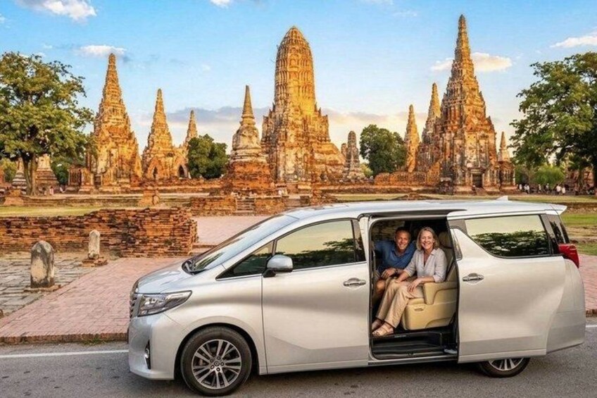 A silver minivan parked in front of ancient temple ruins. 1