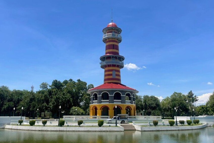 A colorful tower with a red roof and multiple balconies, surrounded by a water feature and greenery. 3