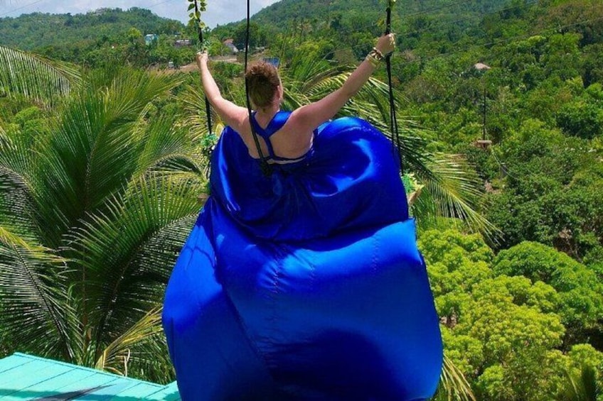 A person in a blue dress swinging on a rope swing over a lush green landscape. 5
